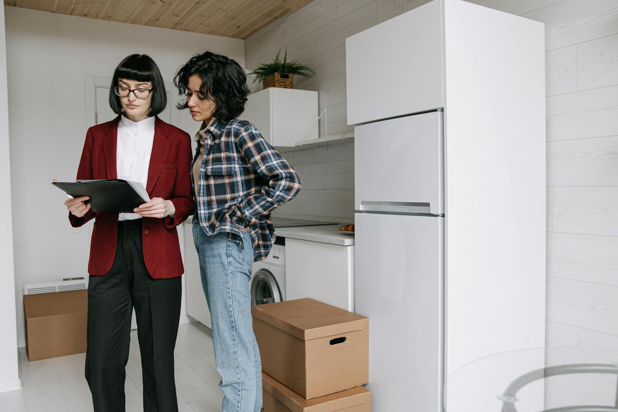 Two women reviewing documents in a kitchen amid moving boxes.